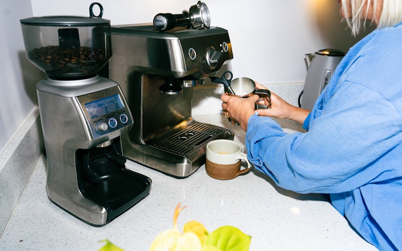 An espresso machine portafilter and filter basket being rinsed under running water with cleaning supplies nearby